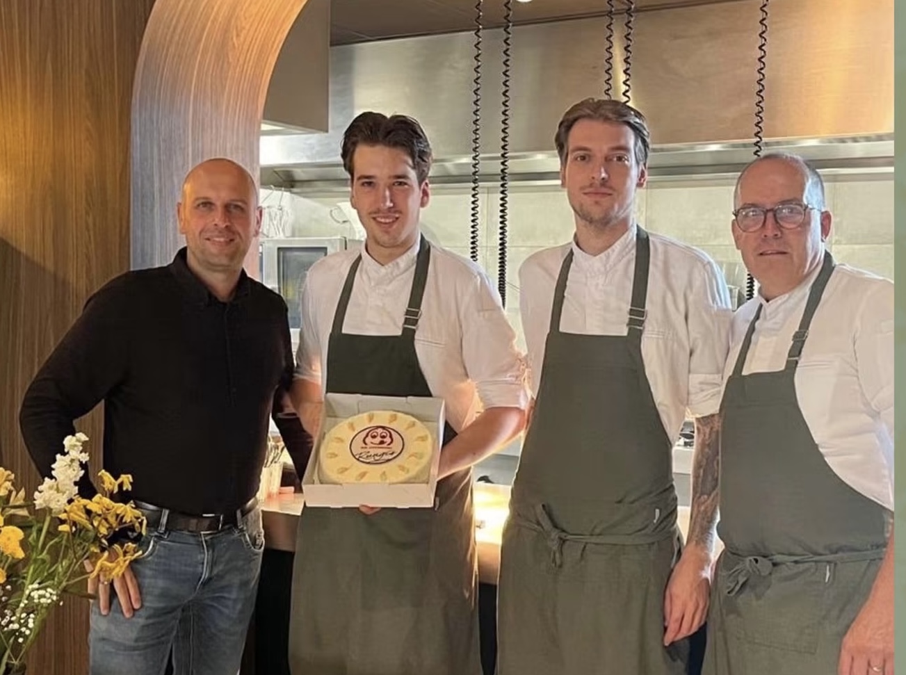 Vier mensen bij de open keuken van Bistro Luux, met een taart waarop het Bib Gourmand-symbool staat