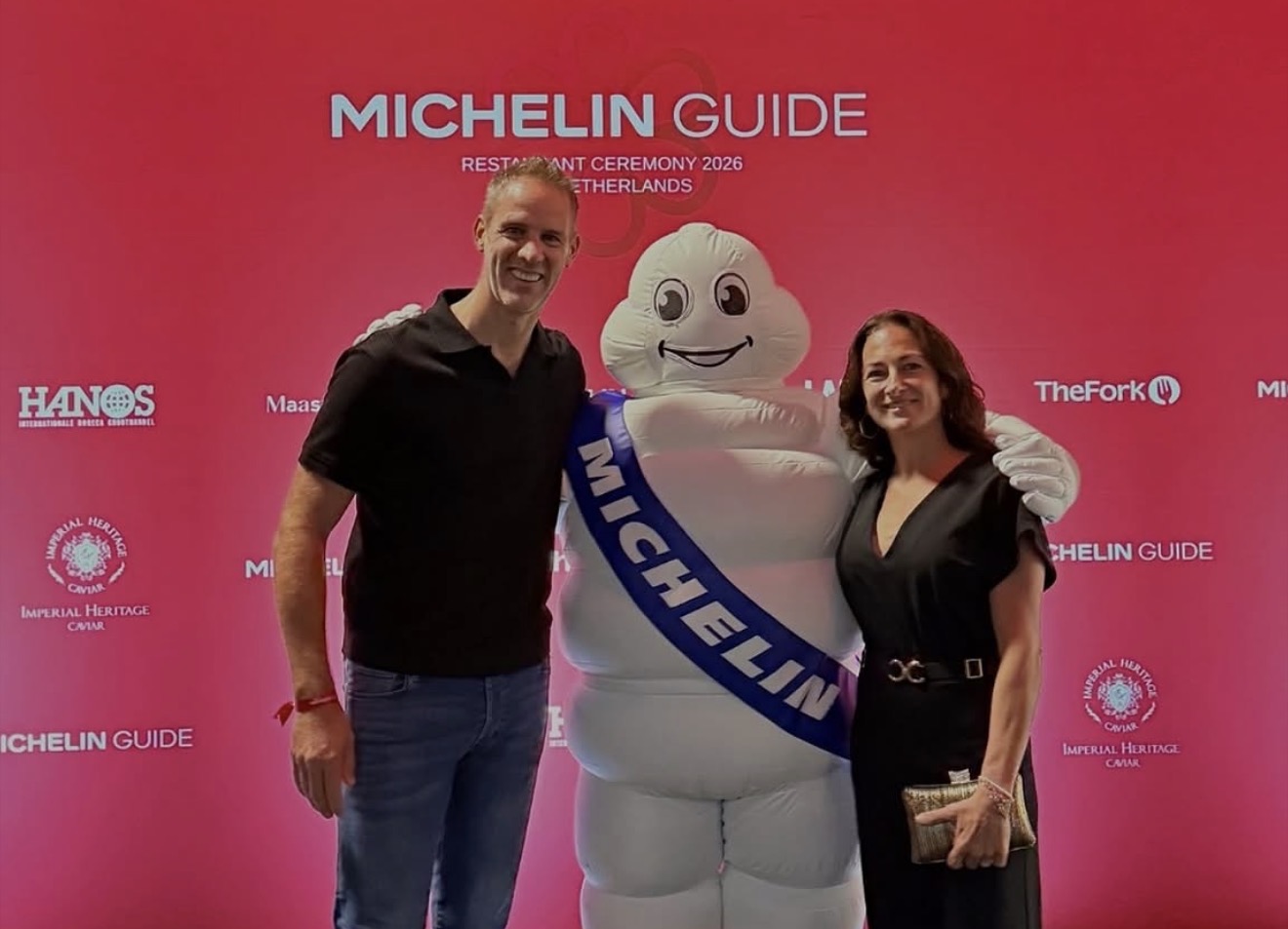 Twee vertegenwoordigers van restaurant ONE met de Michelinmascotte voor de rode achtergrond van de Michelin-presentatie 2026