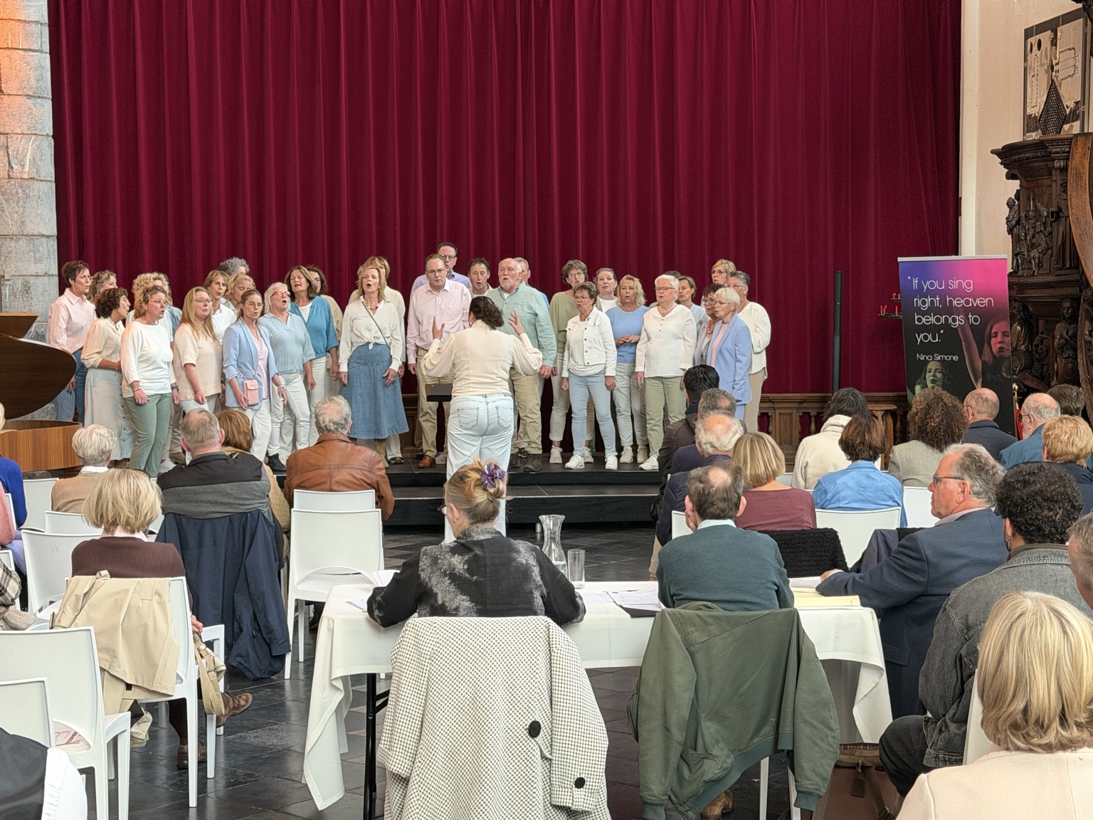 Een koor in lichte kleding zingt voor het publiek in de Paterskerk.