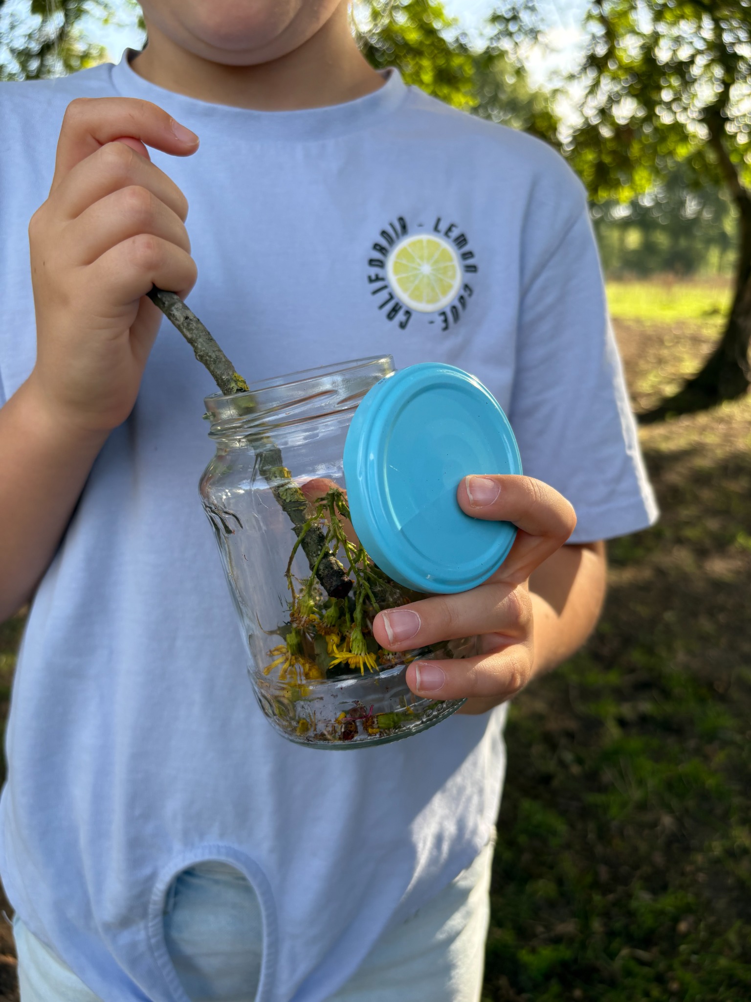 Een leerling maakt natuurparfum van planten in een potje.