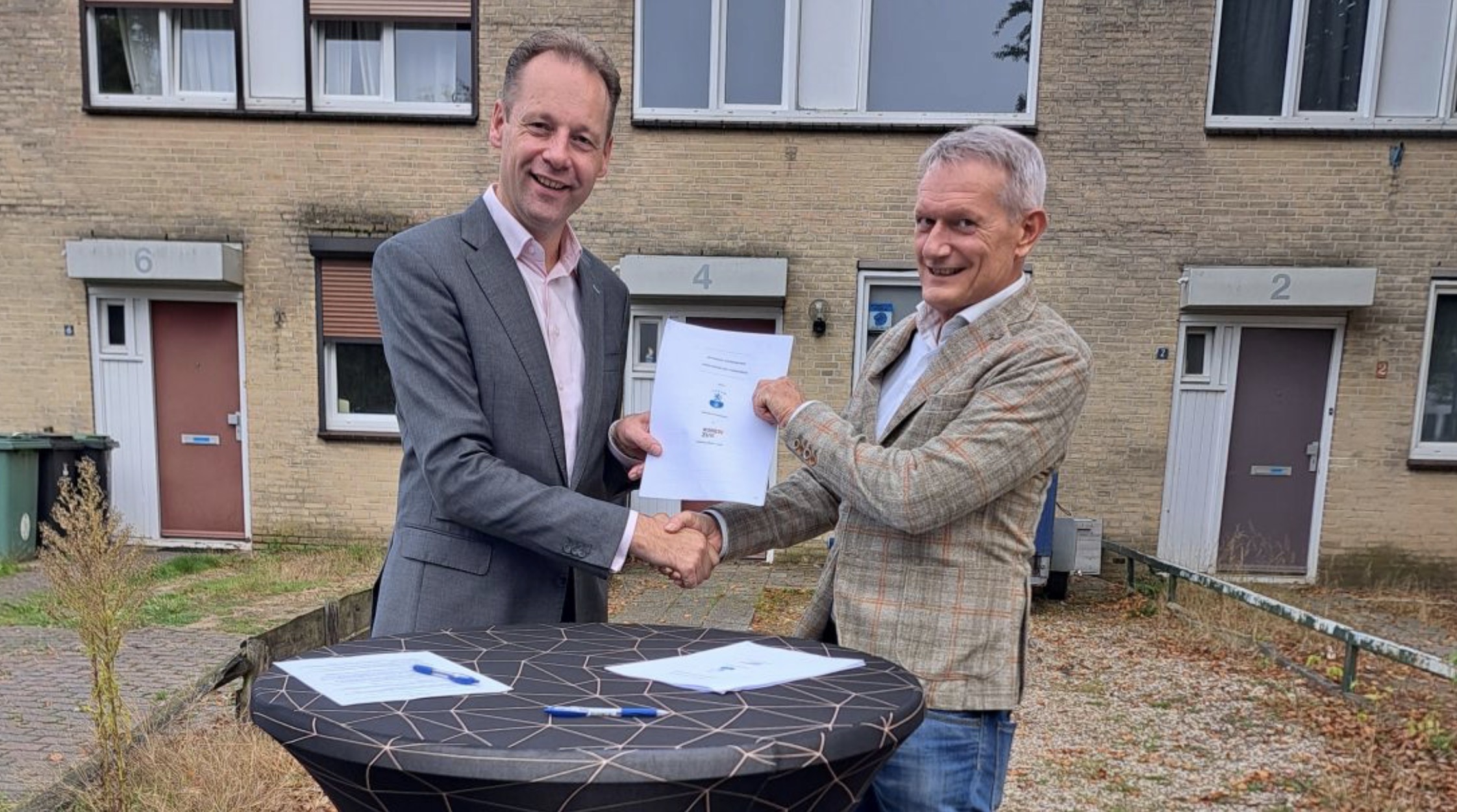 Twee mannen schudden elkaar de hand en tonen de overeenkomst voor de vernieuwing van Sterrenberg, voor de bestaande woningen.